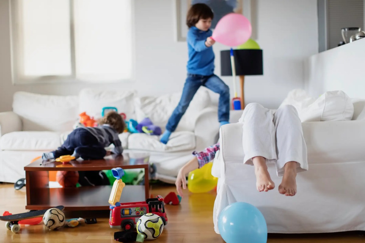 Mutter liegt erschöpft auf der Couch, während ihre Kinder wild drumherum hüpfen