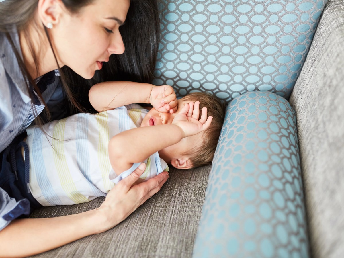 Mutter kümmert sich um müpdes Kind, das auf dem Sofa liegt.