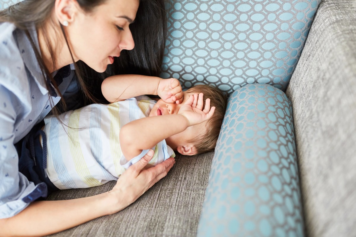 Mutter kümmert sich um müpdes Kind, das auf dem Sofa liegt.