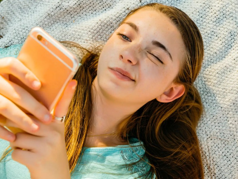 Teenie-Mädchen liegt auf einer Decke und scrollt am Handy.