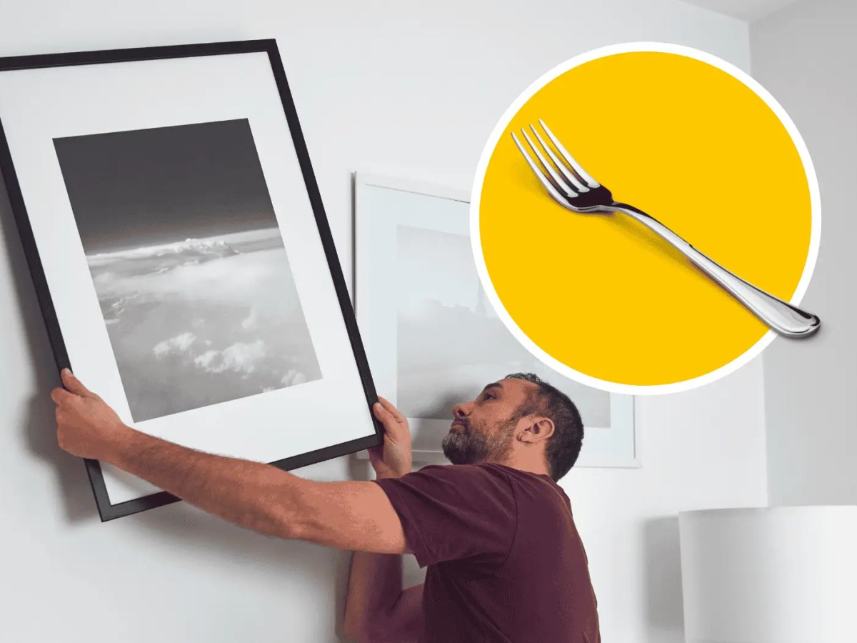Mann hängt Bild an Wand auf.