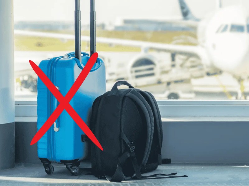 Trolley und Rucksack an Flughafen, der Koffer ist mit rot durchgestrichen.