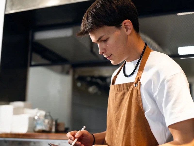 Teenager mit Sch&uuml;rze und Tablet in einem Restaurant.