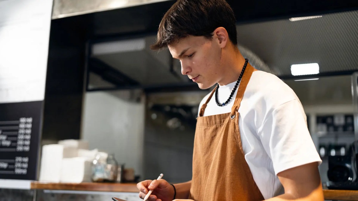 Teenager mit Schürze und Tablet in einem Restaurant.