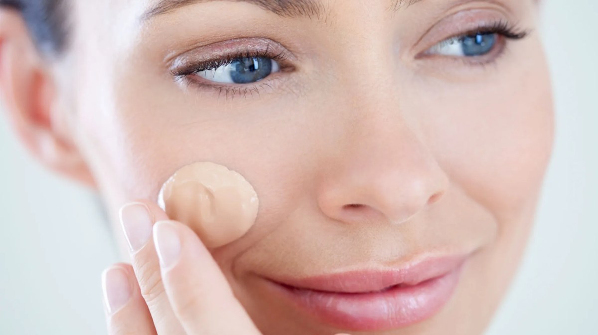 Frau, die sich einen Klecks Make-up ins Gesicht cremt.