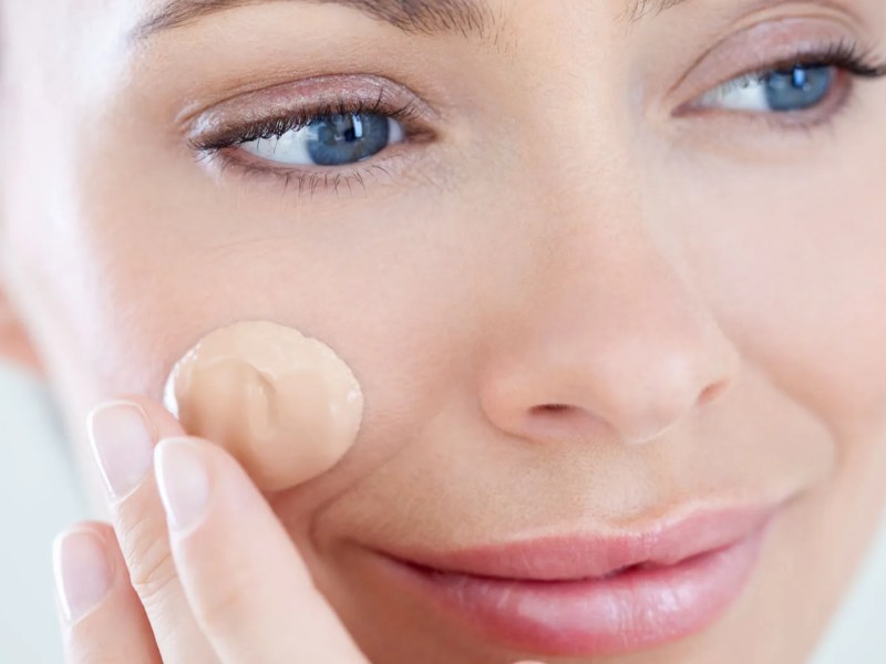 Frau, die sich einen Klecks Make-up ins Gesicht cremt.