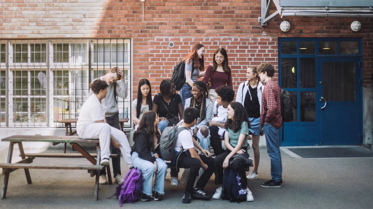Eine Gruppe von Jungen und Mädchen unterschiedlicher Herkunft sitzt während der Pause auf dem Campus der Junior High School.