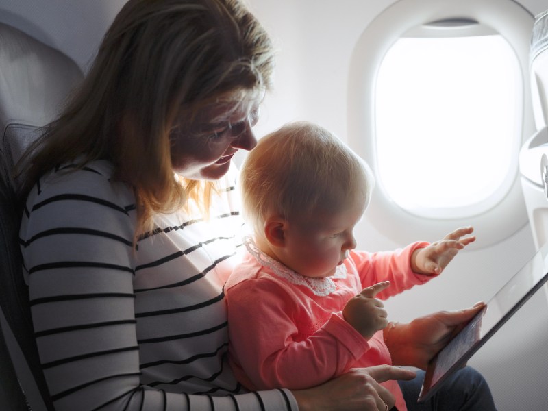 Mutter und Kleinkind sitzen im Flugzeig und schauen auf ein Tablet
