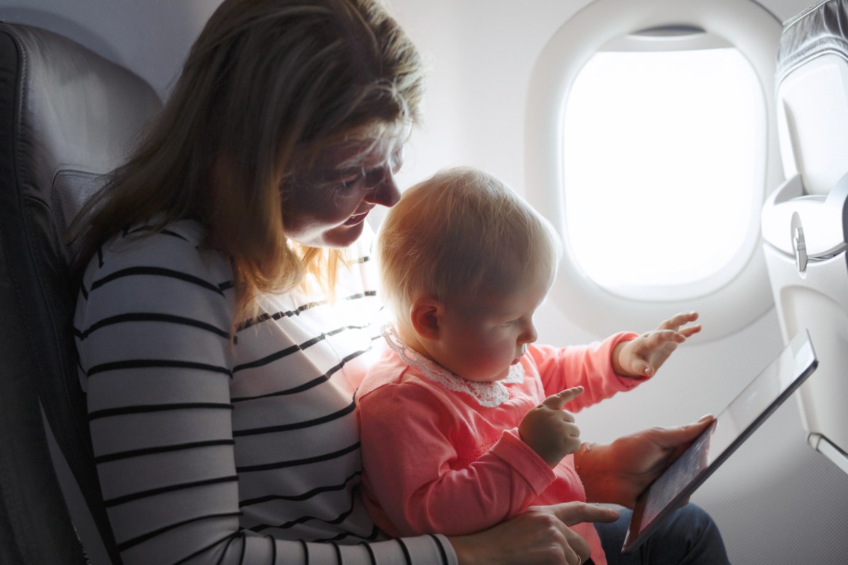 Mutter und Kleinkind sitzen im Flugzeig und schauen auf ein Tablet