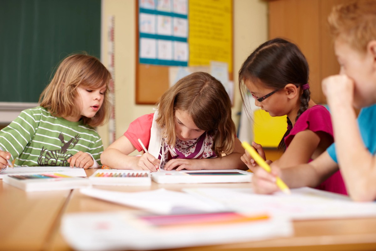 Vier Grundschulkinder sitzen am Schultisch und sehen in ihre Hefte