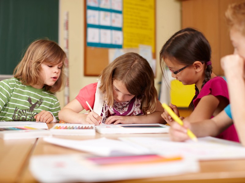 Vier Grundschulkinder sitzen am Schultisch und sehen in ihre Hefte