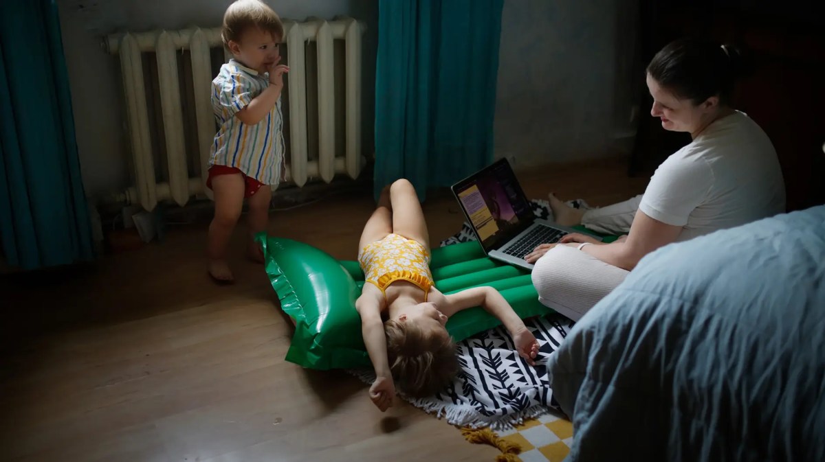 Mutter arbeitet am Laptop, während ihre Kinder um sie herum spielen.