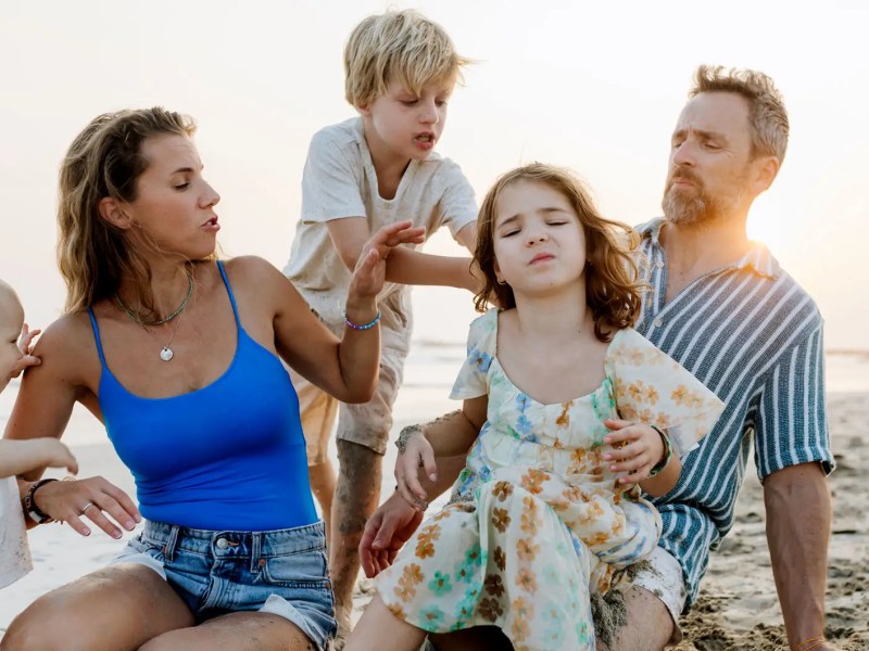 Eltern und drei Kinder am Strand bei Sonnenuntergang.