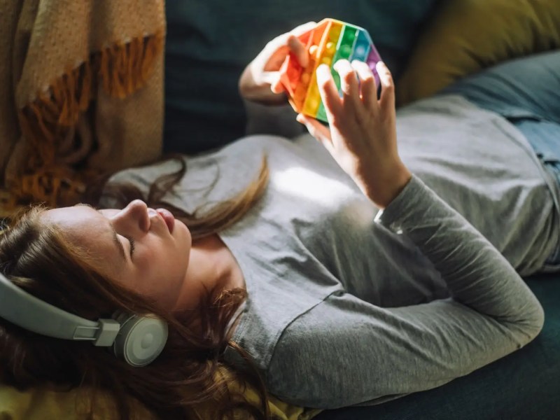 Teenagerin liegt auf dem Sofa mit Kopfhörern und Pop-it.