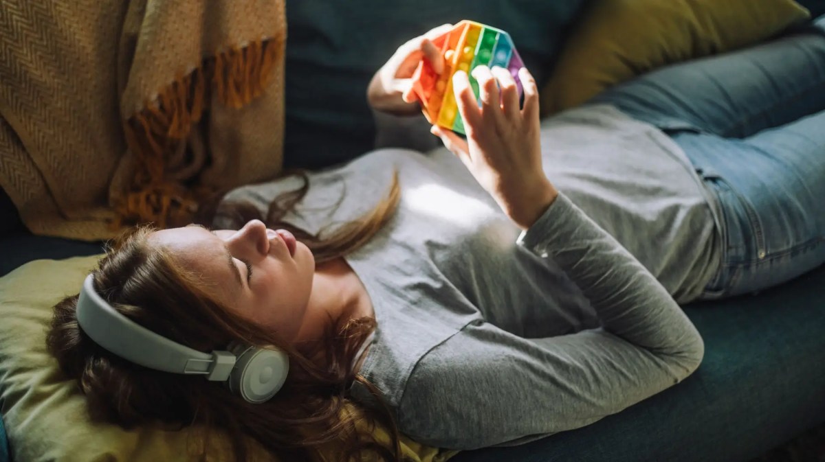 Teenagerin liegt auf dem Sofa mit Kopfhörern und Pop-it.