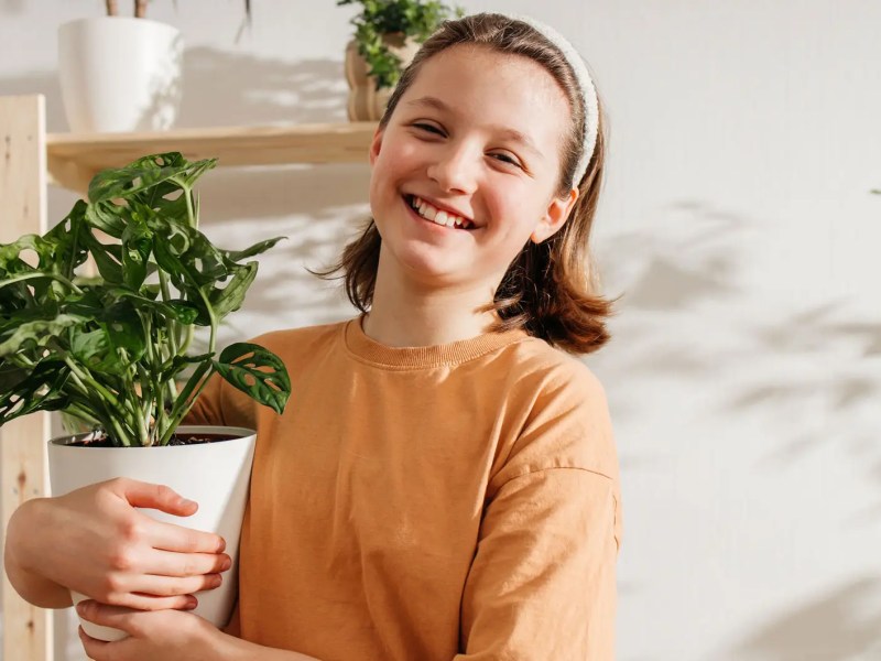Teenagermädchen trägt freudestrahlend einen Blumentopf.
