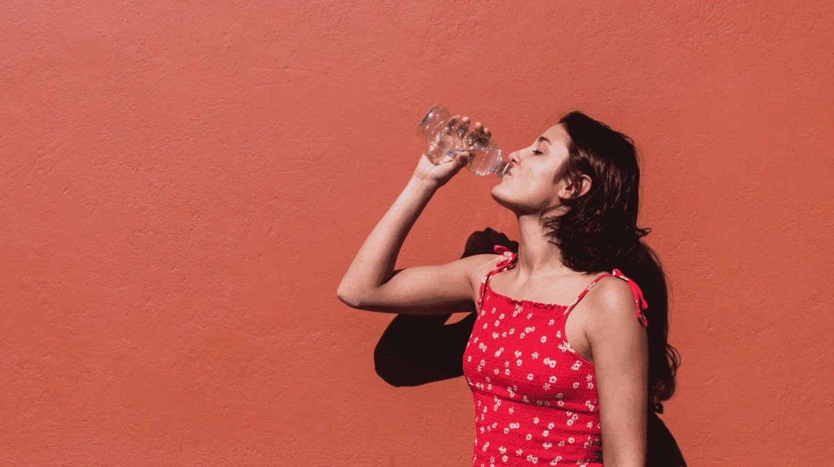 Junge Frau in rotem Top trinkt Wasser an einem Sommertag