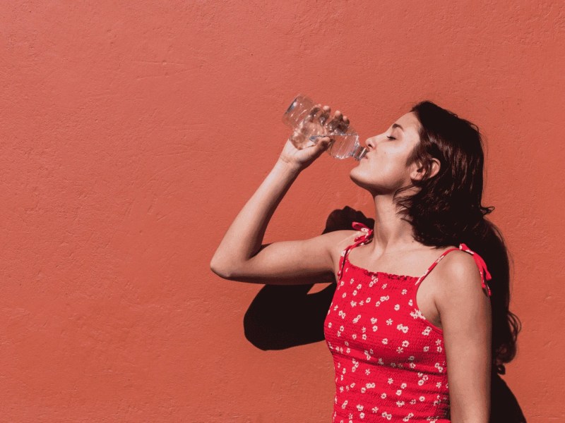 Junge Frau in rotem Top trinkt Wasser an einem Sommertag
