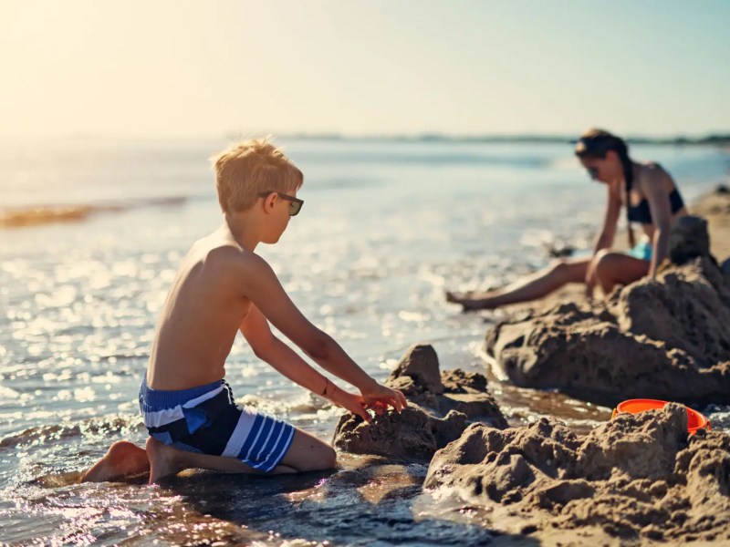 Kinder buddeln mit untergehender Sonne am Strand.