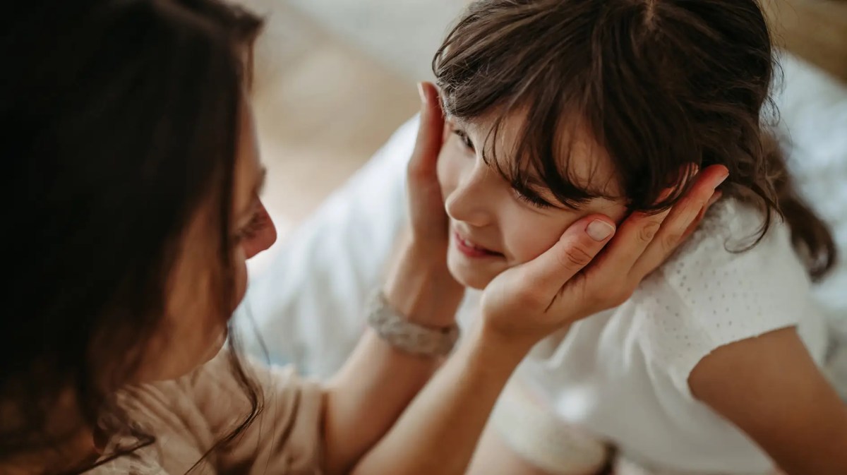 Mutter hält das Gesicht ihrer Tochter, ca. 8 Jahre alt, in den Händen.