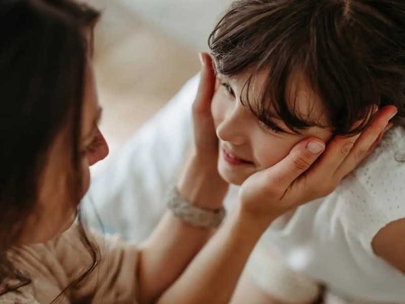 Mutter hält das Gesicht ihrer Tochter, ca. 8 Jahre alt, in den Händen.