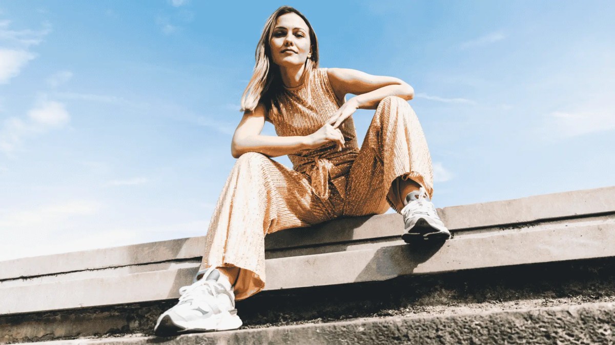 Frau in sommerlichen Jumpsuit sitzt auf Straße.