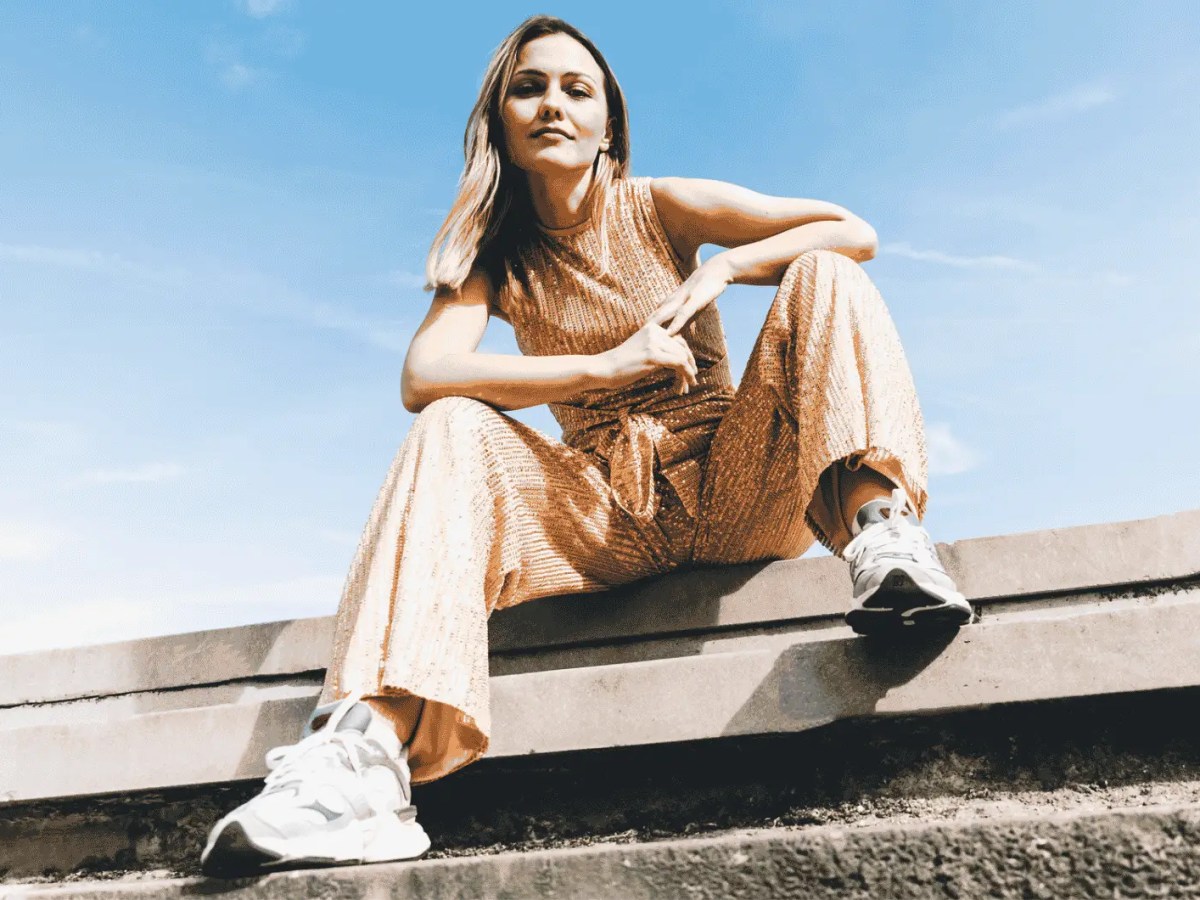 Frau in sommerlichen Jumpsuit sitzt auf Straße.
