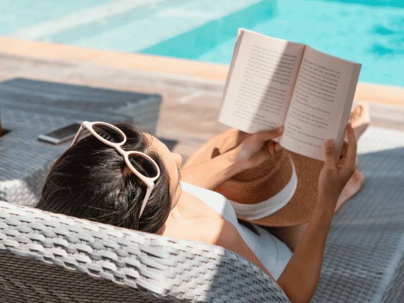 Frau liegt am Pool und liest Buch.