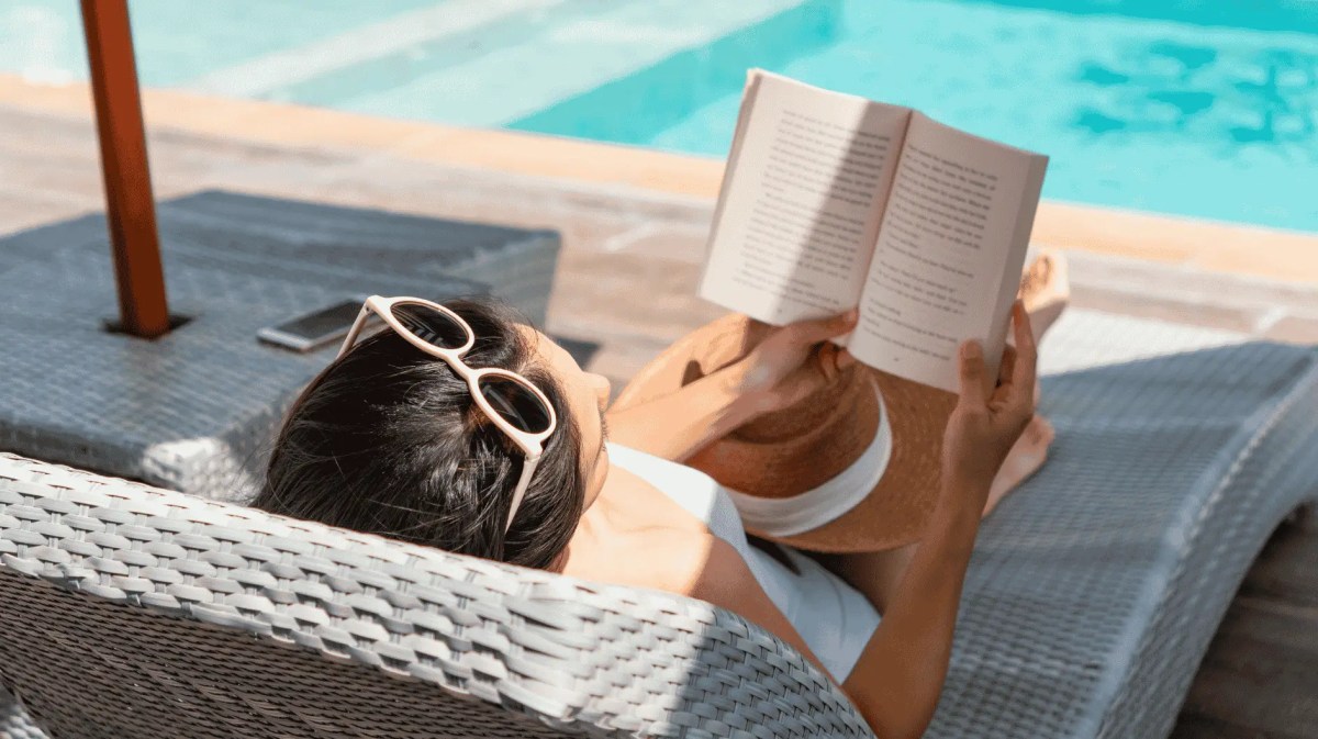 Frau liegt am Pool und liest Buch.