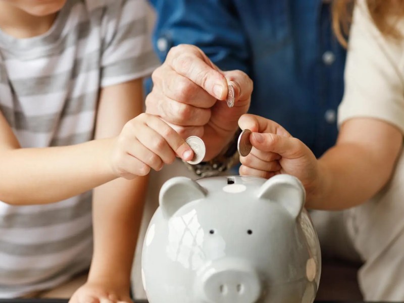 Mann und zwei Kinder werfen Geld in ein Sparschwein.
