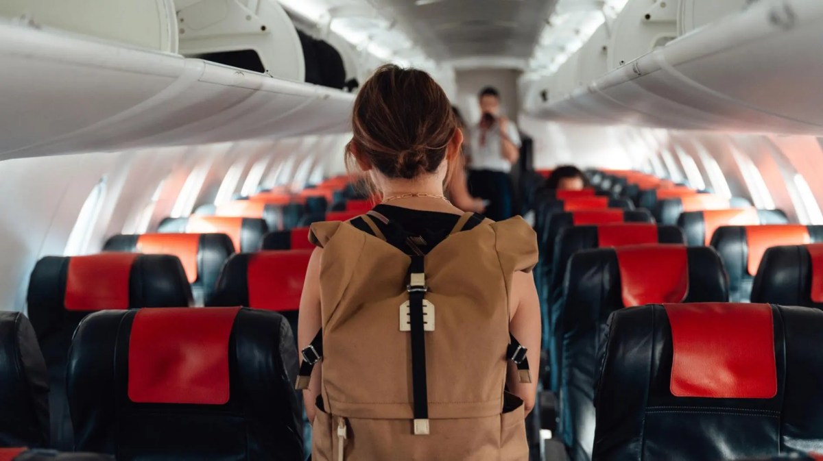 Frau mit Rucksack von hinten läuft durch ein Flugzeug.