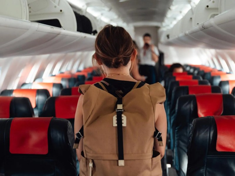Frau mit Rucksack von hinten läuft durch ein Flugzeug.