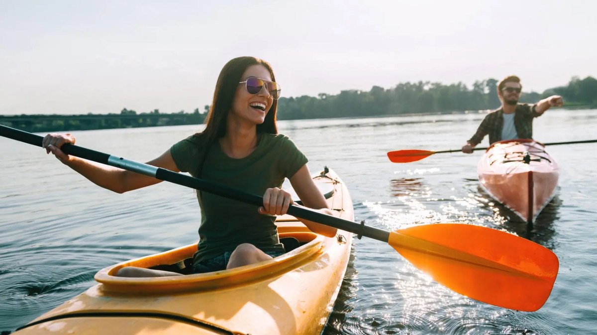 Vorne rechts ist eine Frau in einem Kajak auf dem See, dahinter ein Mann. Beide haben Spaß.