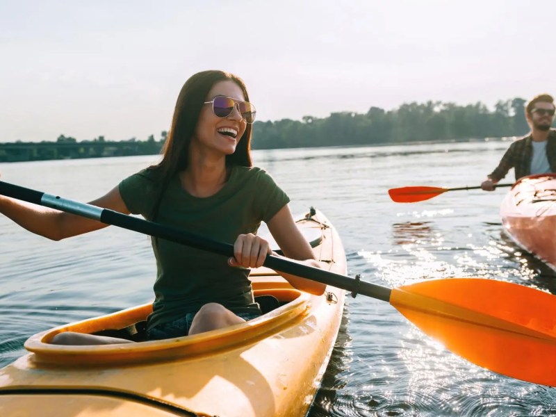 Vorne rechts ist eine Frau in einem Kajak auf dem See, dahinter ein Mann. Beide haben Spaß.