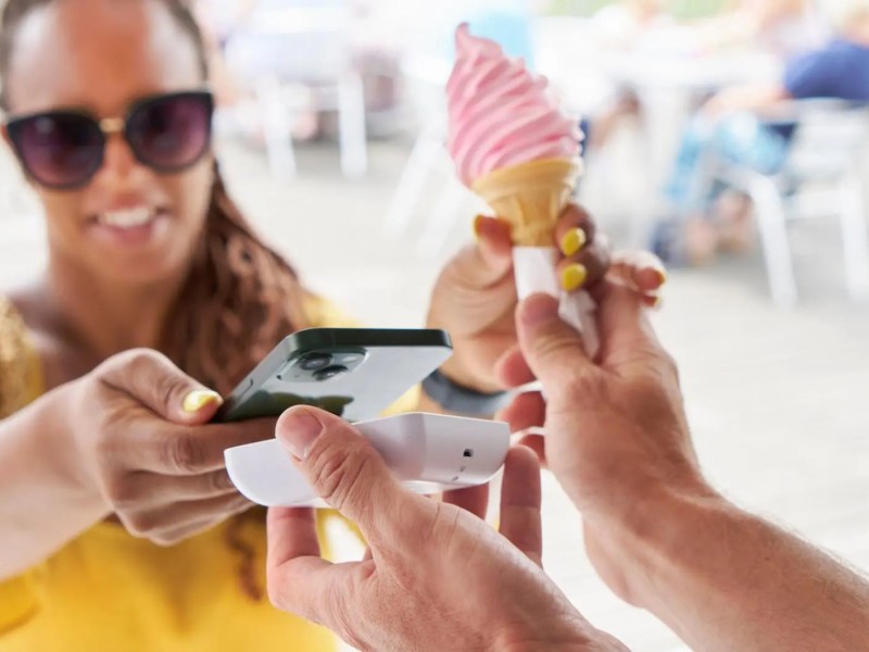 Frau bezahlt ein Eis an einem Stand draußen.